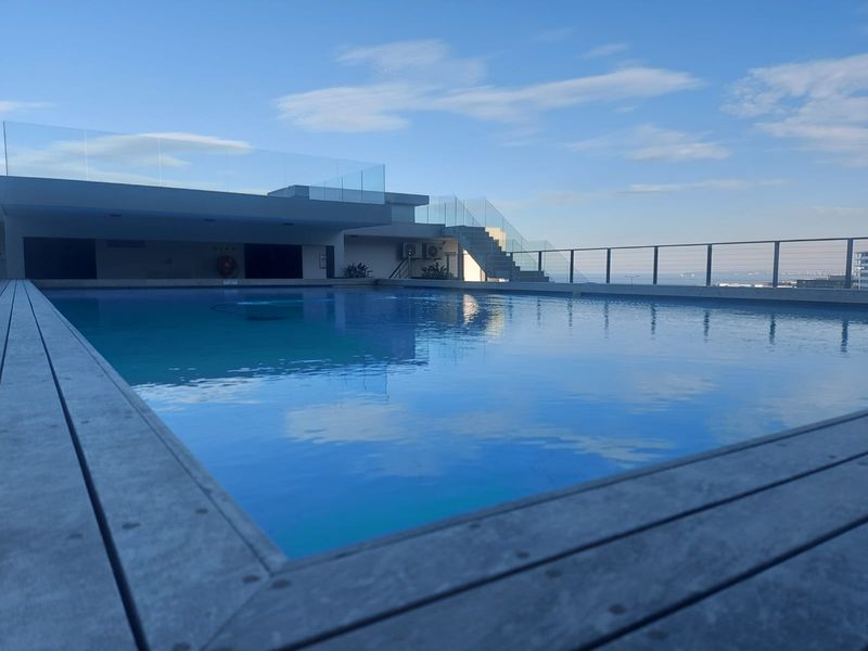 A modern rooftop swimming pool featuring glass balustrades, timber decking, and expansive views, providing a premium outdoor leisure space for residents.