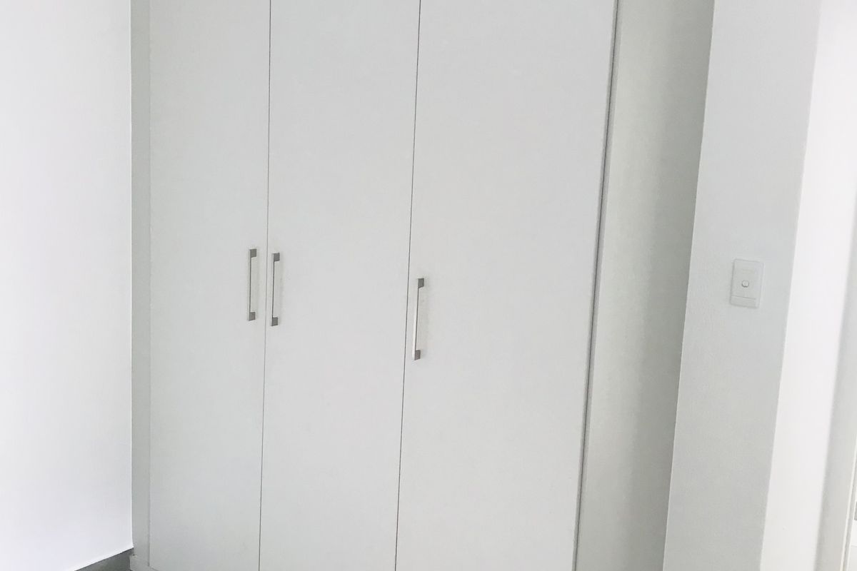A clean, modern bedroom featuring a large, white built-in wardrobe with sleek metal handles and neutral floor tiling.