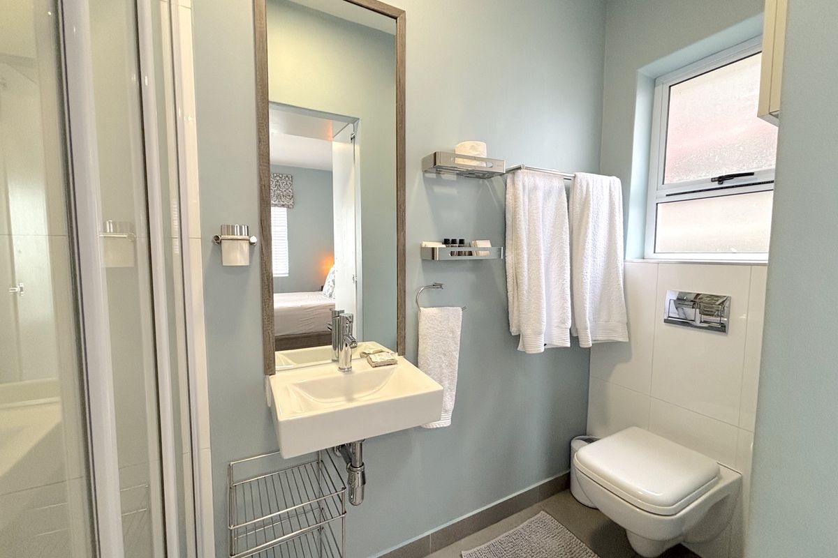 A compact, modern bathroom featuring a wall-mounted basin, a concealed cistern toilet, and a glass-enclosed shower with light blue wall finishes.