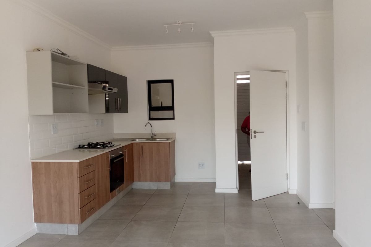 A modern, clean kitchen featuring light wood-tone cabinetry, a built-in oven, gas hob, extractor fan, and tiled flooring in an open-plan layout.