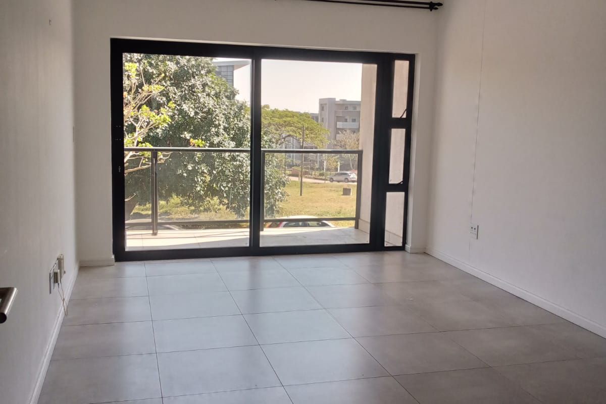 A bright, empty living area featuring large sliding glass doors that open onto a balcony, finished with neutral floor tiles.