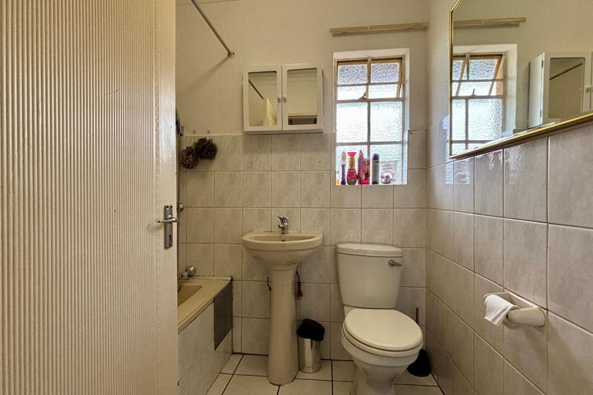 A compact bathroom featuring a pedestal basin, toilet, and a built-in bathtub with tiled walls and flooring.