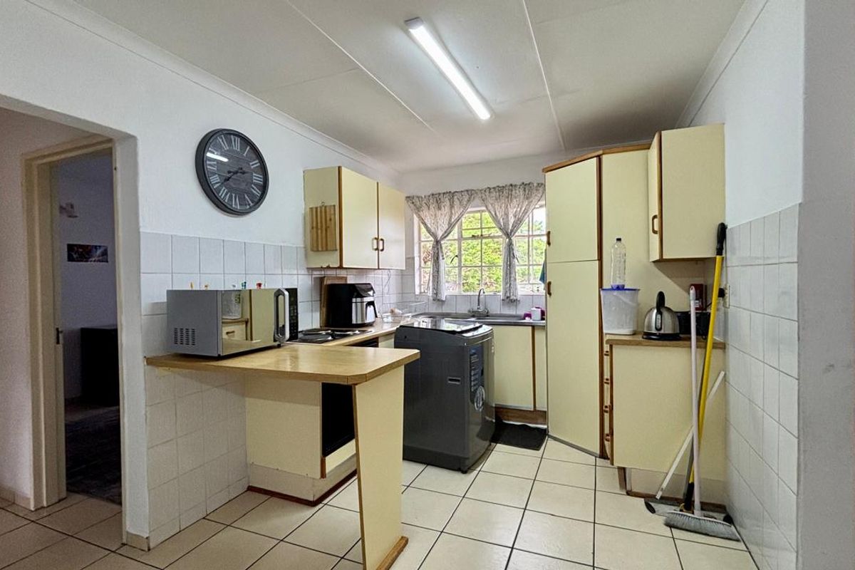 A functional kitchen featuring tiled flooring, built-in cabinetry, a stainless steel sink, and tiled splashbacks, offering a practical layout for daily meal preparation.