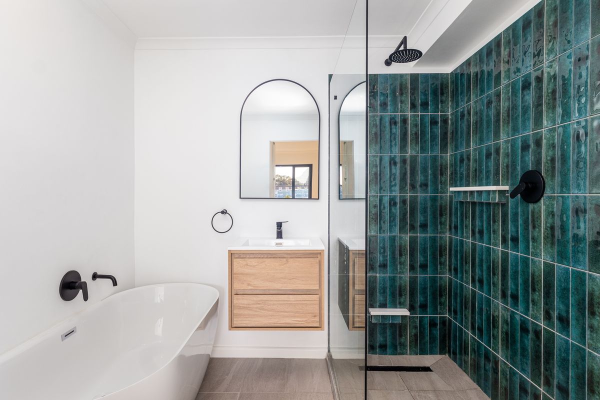 Modern bathroom featuring a freestanding bathtub, wall-mounted timber vanity, and a walk-in shower with striking teal vertical feature tiles and matte black fixtures.