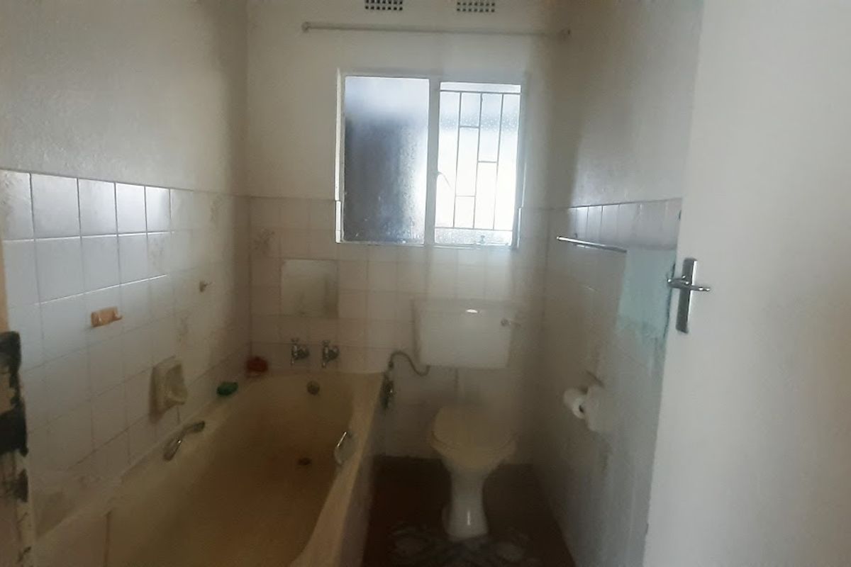 A dated bathroom featuring a standard bathtub, toilet, and tiled walls. The space requires modernization and cosmetic updates to improve its overall condition.