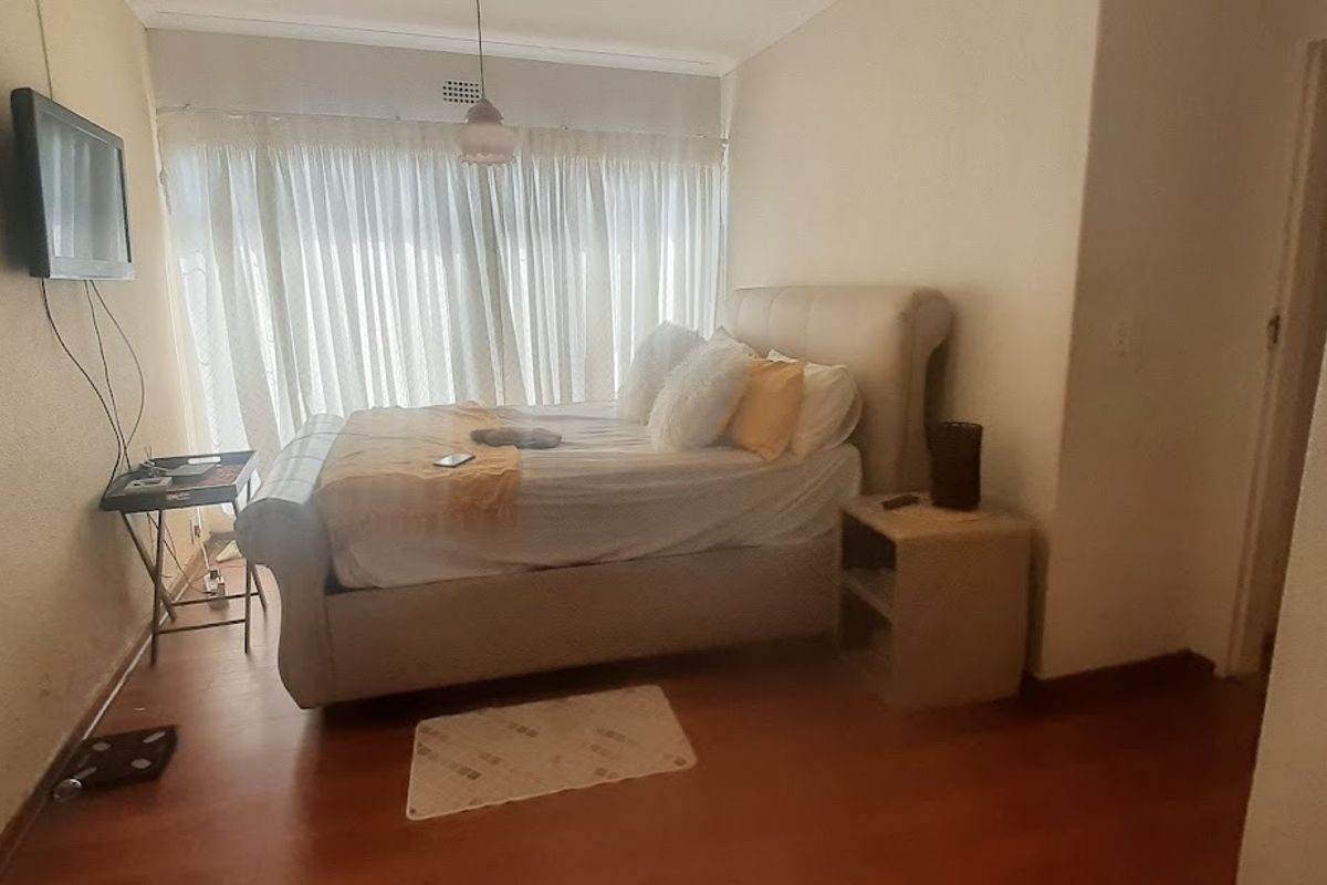 A bedroom featuring laminate flooring, a large window with curtains, and a neutral color palette, offering a functional and comfortable living space.