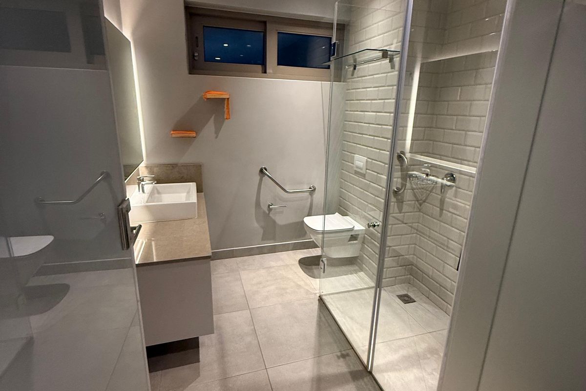 Modern bathroom featuring a glass-enclosed walk-in shower, wall-mounted toilet, floating vanity with basin, and neutral floor tiling.
