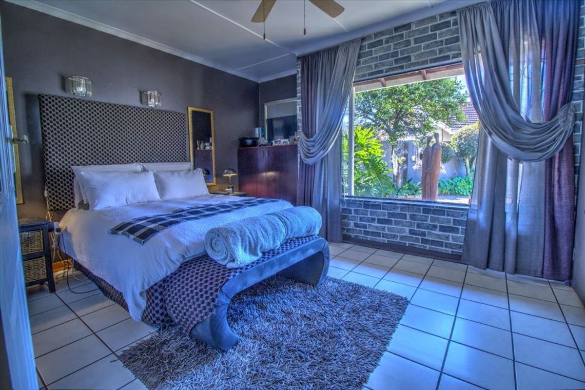 A bedroom featuring tiled flooring, a brick feature wall, and a large window overlooking the garden.