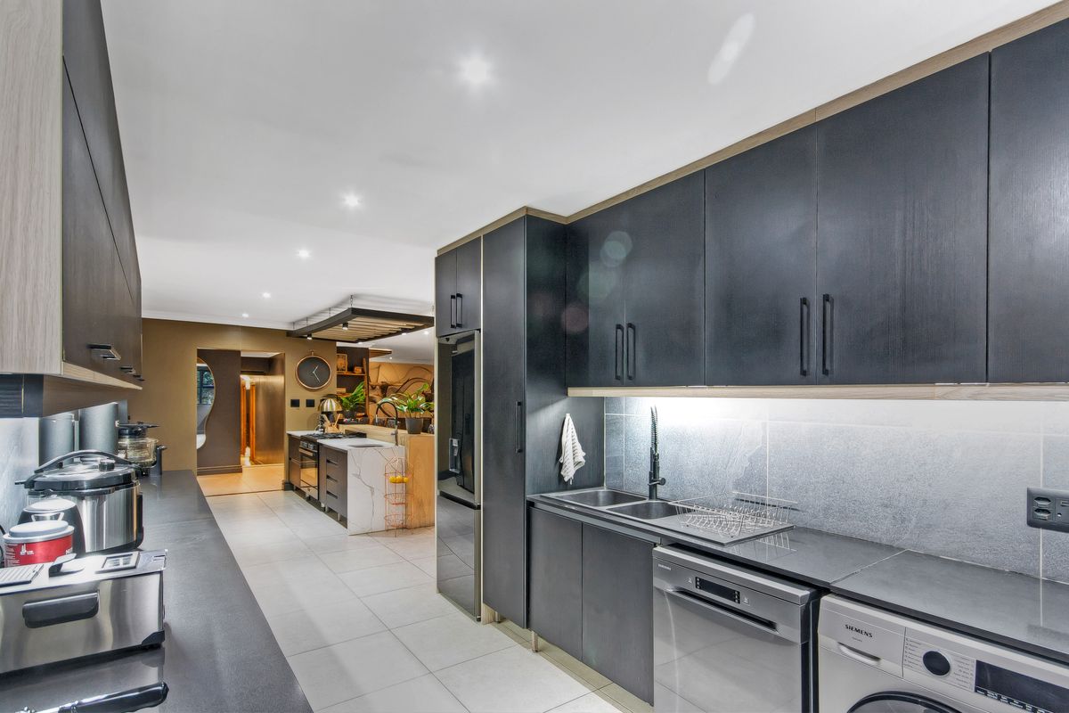 Modern kitchen featuring dark cabinetry, stone countertops, integrated appliances, and a seamless transition into the adjacent living area.