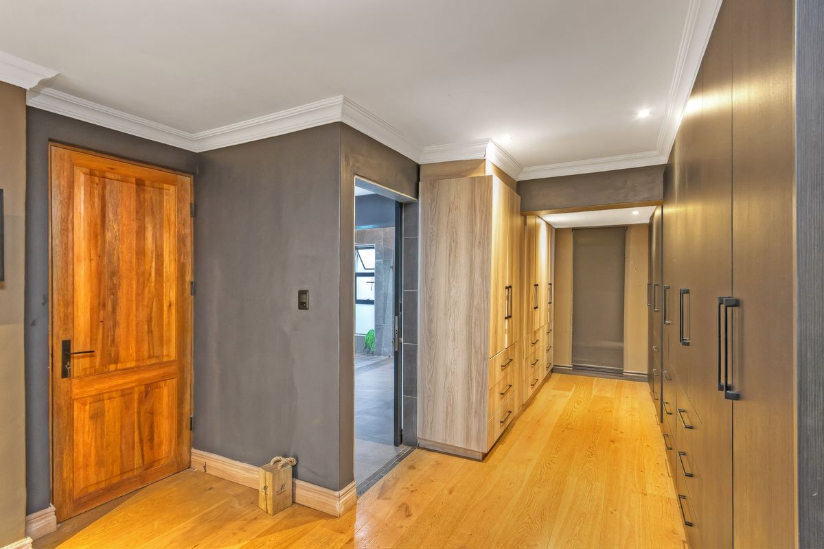 A well-appointed dressing room featuring extensive built-in cabinetry, warm timber flooring, and crown molding, providing ample storage space.