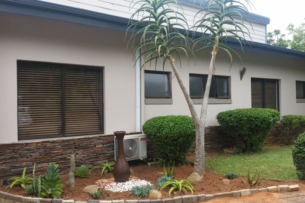 A well-maintained exterior rear elevation featuring stone cladding accents, landscaped garden beds, and integrated air conditioning unit.