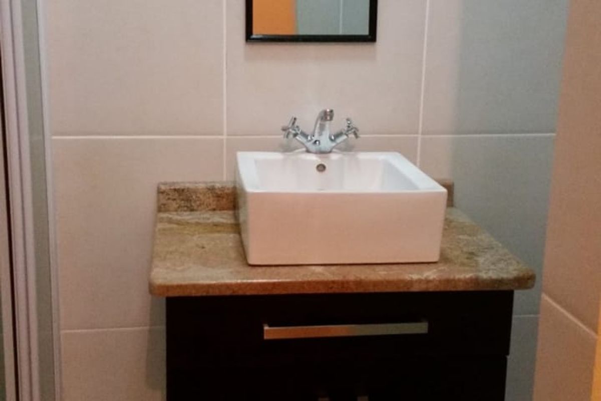 A modern bathroom vanity featuring a square vessel sink, stone countertop, and dark wood cabinetry with chrome hardware, set against tiled walls.