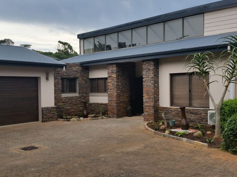 Front exterior view of a modern house featuring stone cladding, a paved driveway, and an attached garage.
