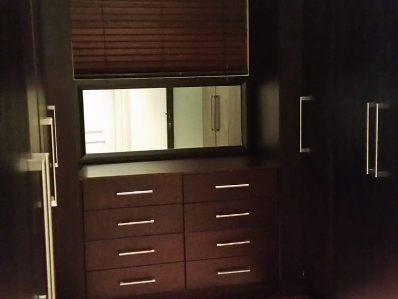 A walk-in closet featuring dark wood cabinetry, built-in drawers, and integrated shelving with a central mirror and window.
