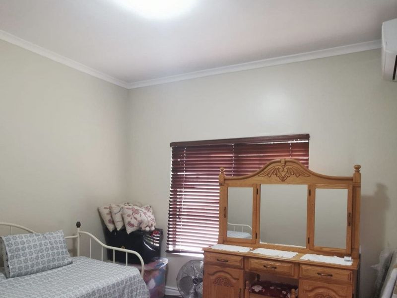 A bedroom featuring timber flooring, wooden venetian blinds, and a wall-mounted air conditioning unit.