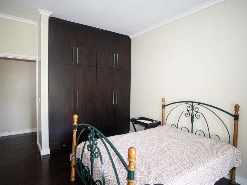 A bedroom featuring dark wood built-in cupboards and dark laminate flooring, providing ample storage and a neutral aesthetic.