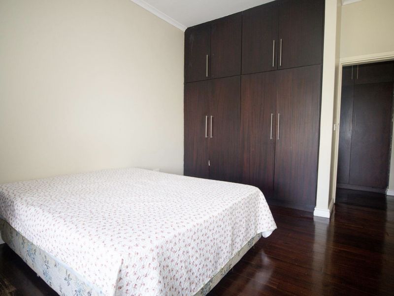 A well-maintained bedroom featuring dark wood flooring and extensive floor-to-ceiling built-in cupboards providing ample storage space.