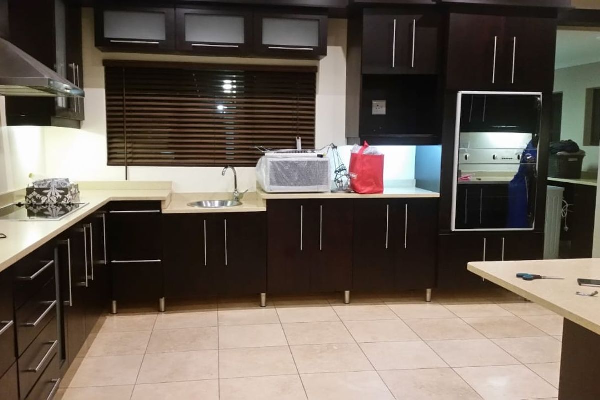 Modern kitchen featuring dark cabinetry, light-toned countertops, integrated oven, stainless steel extractor fan, and tiled flooring.