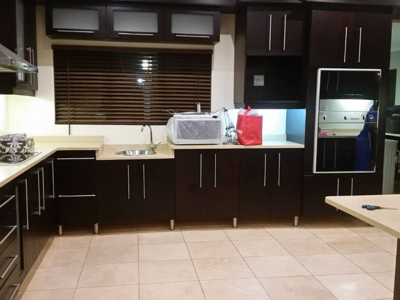 Modern kitchen featuring dark cabinetry, light-toned countertops, integrated oven, stainless steel extractor fan, and tiled flooring.