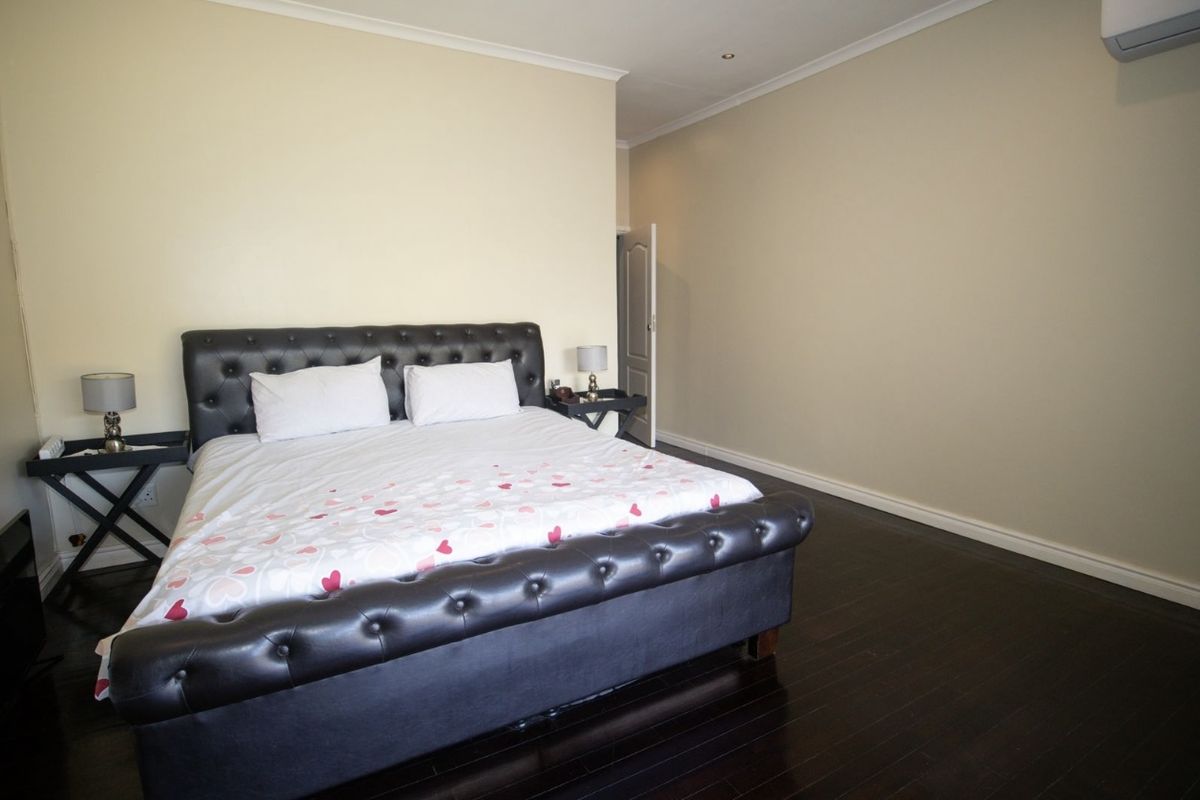 Spacious bedroom featuring dark wood flooring, neutral wall tones, and a wall-mounted air conditioning unit.