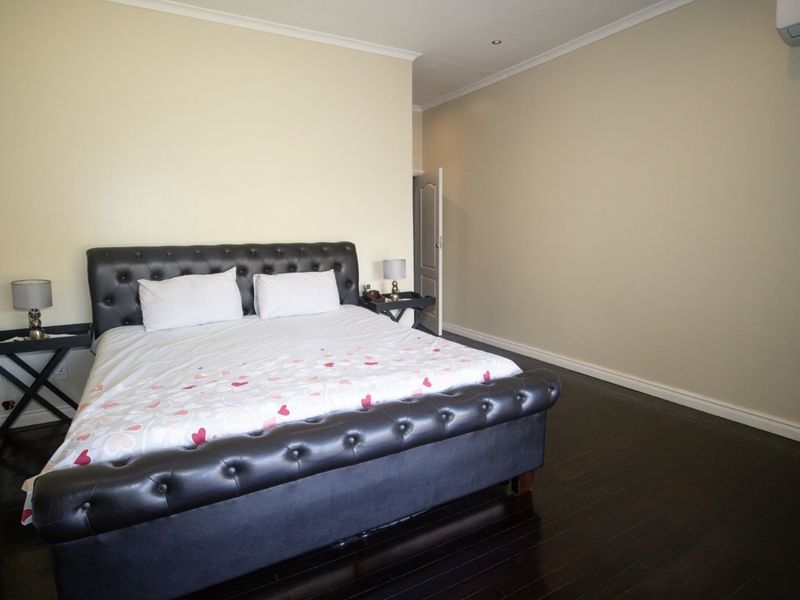 Spacious bedroom featuring dark wood flooring, neutral wall tones, and a wall-mounted air conditioning unit.