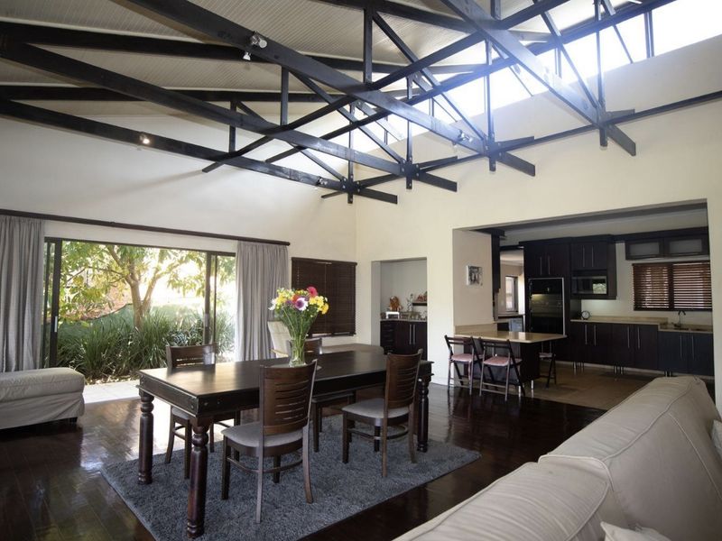Spacious open-plan living and dining area featuring high vaulted ceilings with exposed timber trusses, large sliding doors to the garden, and an integrated kitchen.