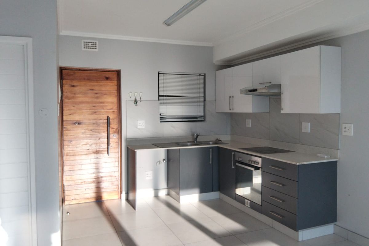 A clean, modern kitchen featuring two-tone cabinetry, built-in oven and hob, tiled backsplash, and neutral floor tiles in an open-plan layout.