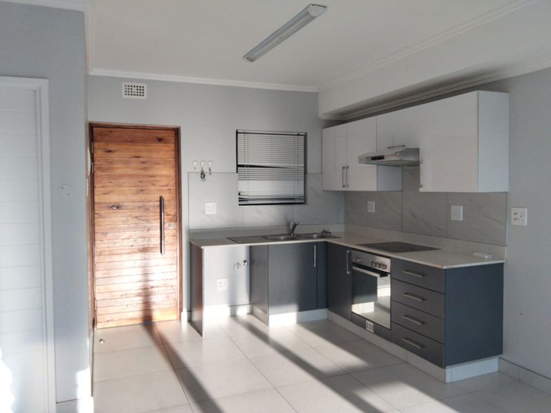 A clean, modern kitchen featuring two-tone cabinetry, built-in oven and hob, tiled backsplash, and neutral floor tiles in an open-plan layout.