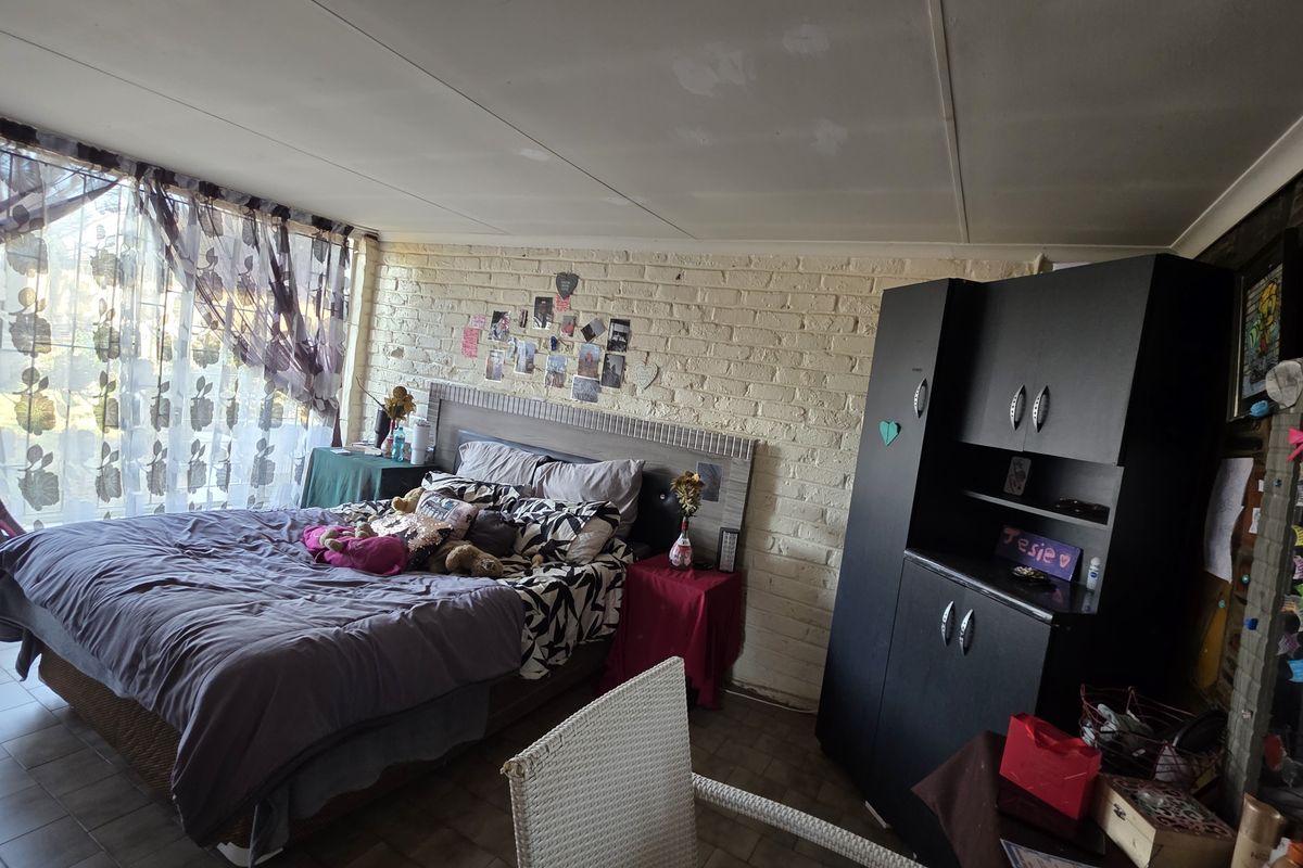 A bedroom featuring painted brick walls, tiled flooring, and ceiling panels, offering a functional space with potential for cosmetic updates.