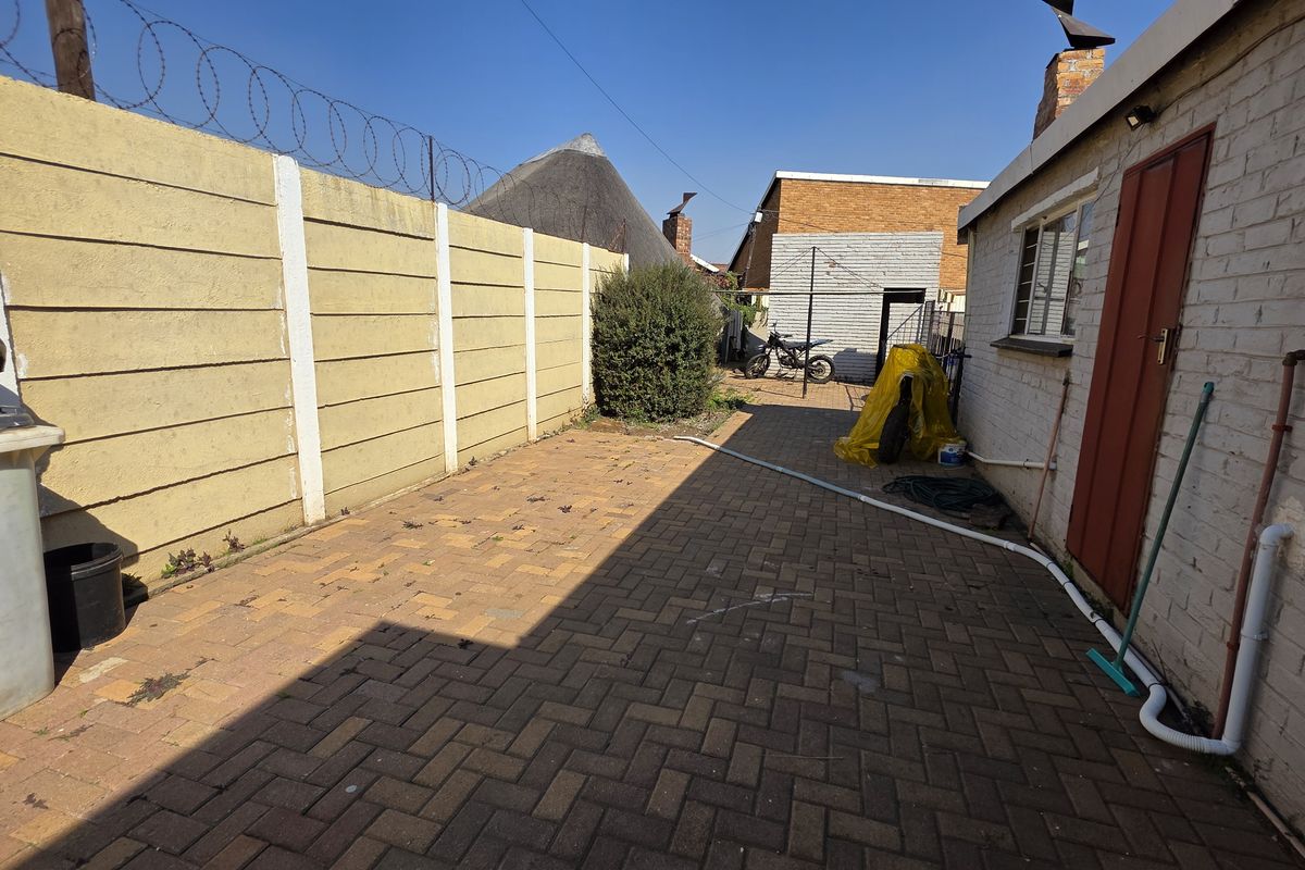 A paved rear courtyard area featuring a precast concrete boundary wall with security razor wire and exposed exterior brickwork.