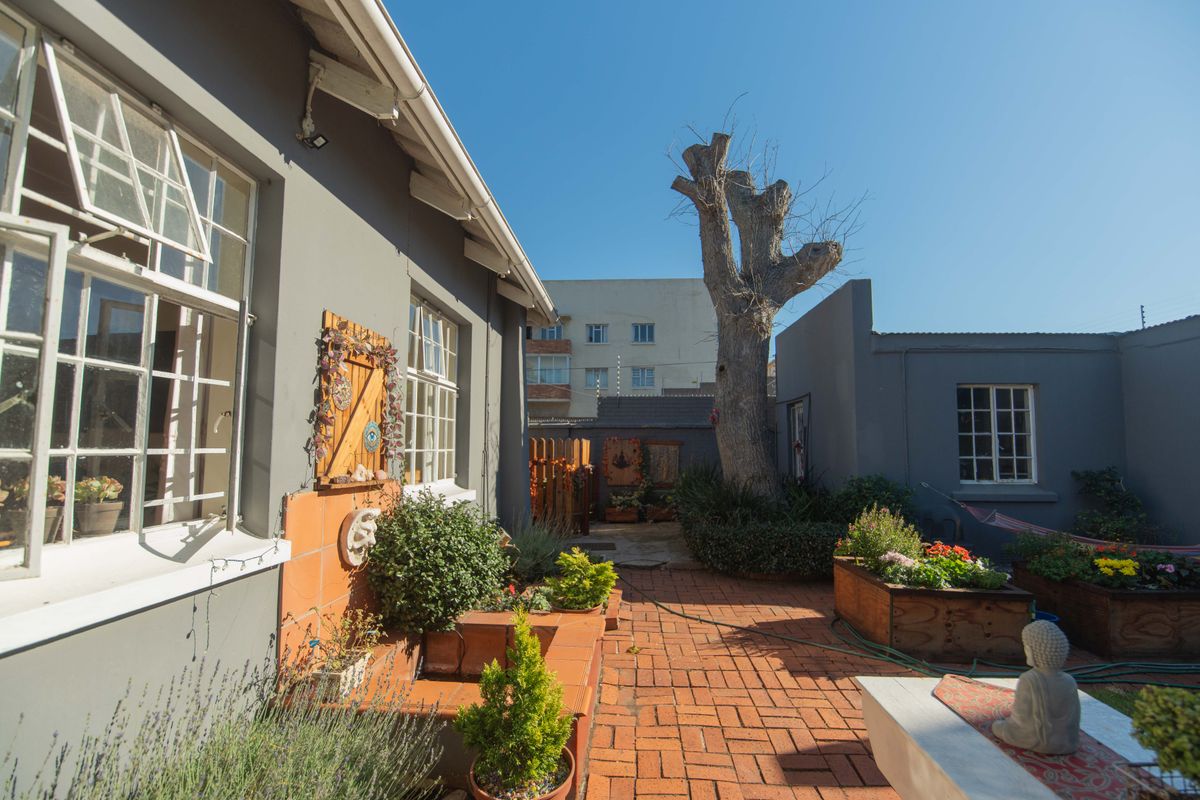 A private rear courtyard featuring brick paving, established garden beds, and a mature tree, providing a quiet outdoor space adjacent to the home.