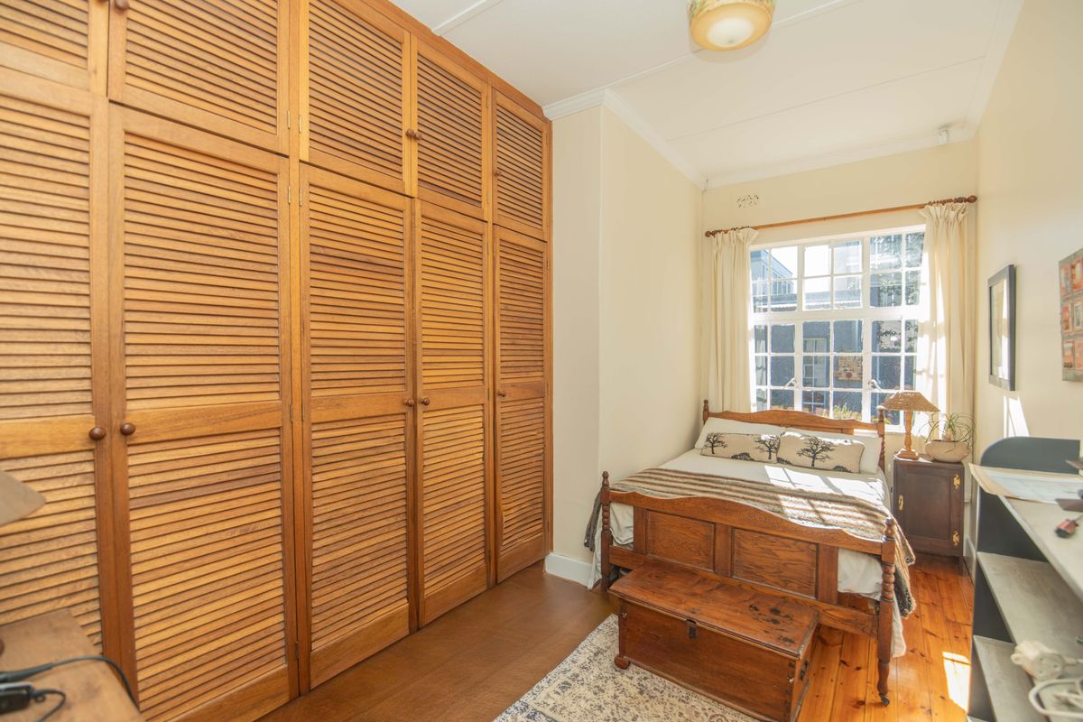 A bedroom featuring extensive floor-to-ceiling wooden louvered built-in cupboards and polished timber flooring.