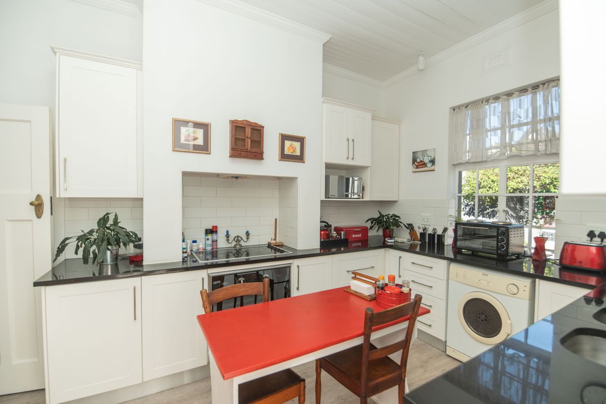 A bright kitchen featuring white cabinetry, black countertops, a built-in hob, and a tiled backsplash, offering a clean and functional workspace.
