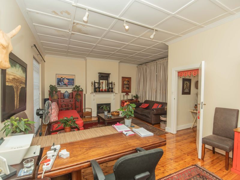 A living room featuring a fireplace, wooden flooring, and a coffered ceiling, currently utilized as a multi-purpose living and workspace area.