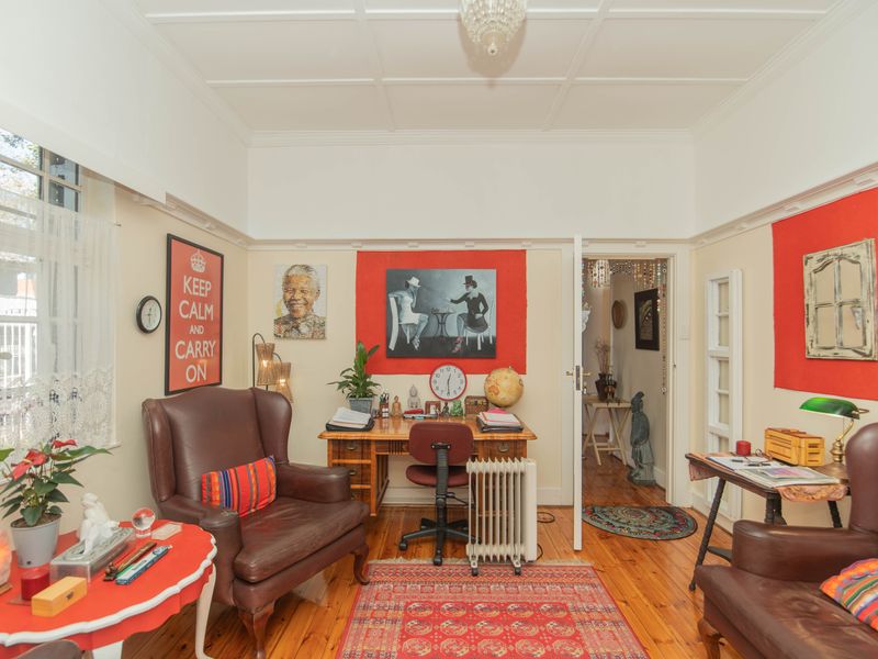 A cozy living room featuring original timber flooring, high ceilings with decorative molding, and a classic doorway leading to the hallway.