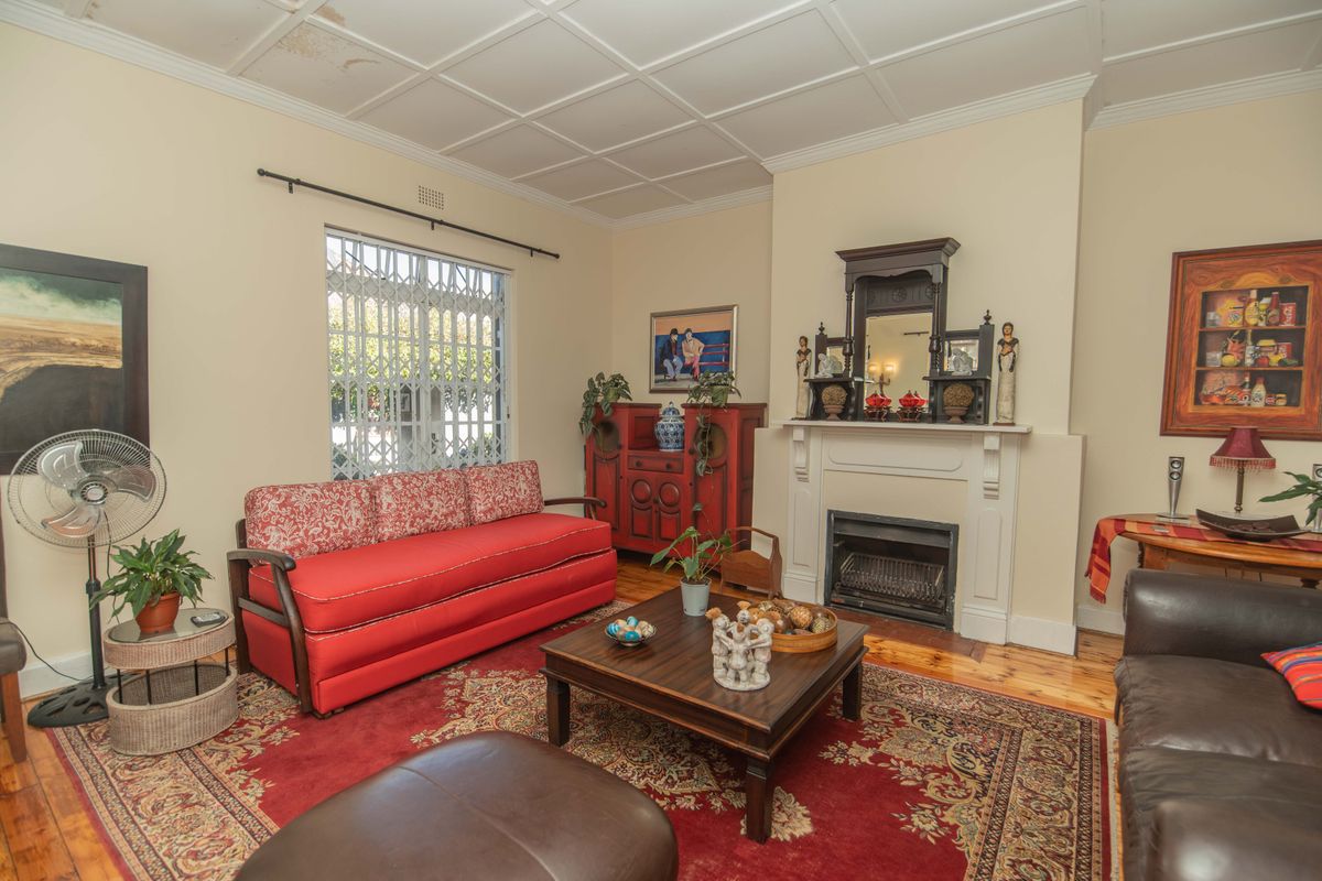 A traditional living room featuring a built-in fireplace with a mantelpiece, timber flooring, and a security gate on the window.