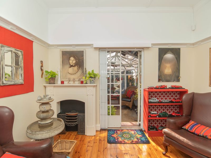 A cozy living room featuring a traditional fireplace, polished timber flooring, and classic crown molding, with direct access to an adjoining sunroom.
