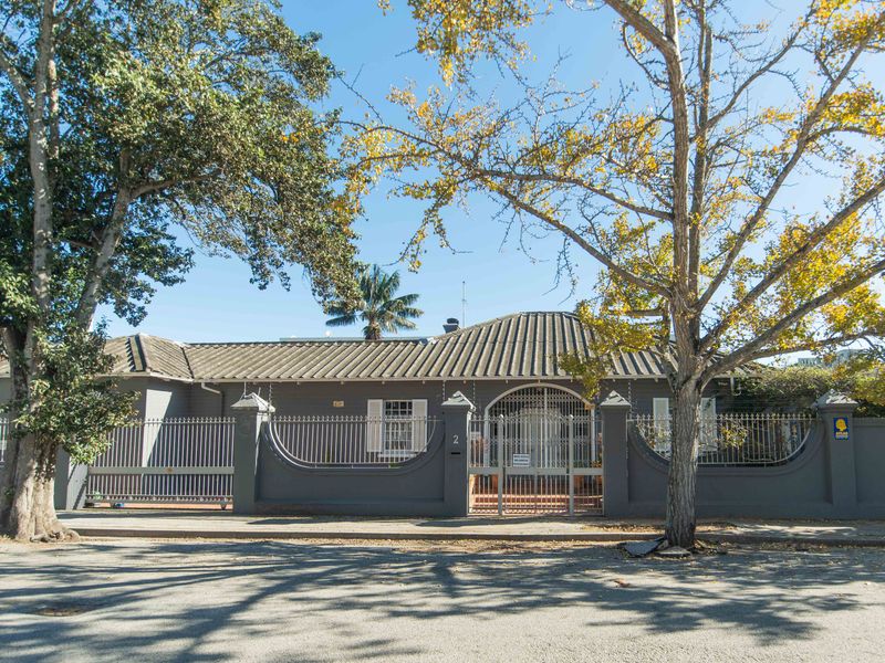 Front elevation of a single-story house featuring a tiled roof, secure perimeter wall with metal fencing, and a gated entrance.