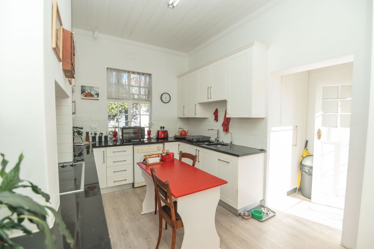 A bright kitchen featuring white cabinetry, black stone countertops, a tiled backsplash, and light-toned laminate flooring with direct access to an outdoor area.