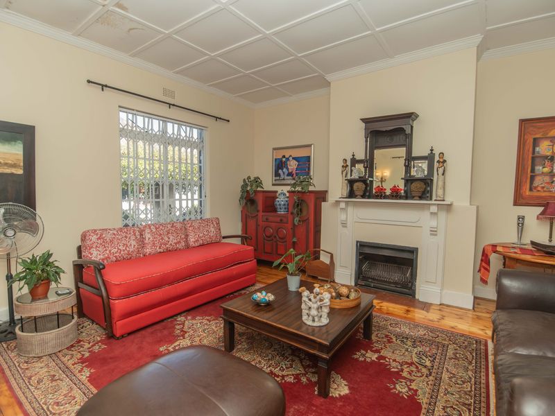 A traditional living room featuring a fireplace with a mantelpiece, timber flooring, and a tiled ceiling with visible signs of water damage.