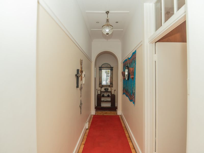 A classic hallway featuring timber flooring, an elegant archway, and traditional picture rails, leading towards a bright rear entrance.