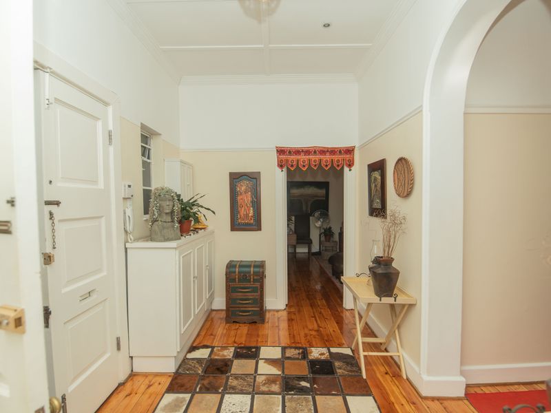 A bright and welcoming hallway featuring polished hardwood flooring, classic archway detailing, and built-in storage cabinetry.