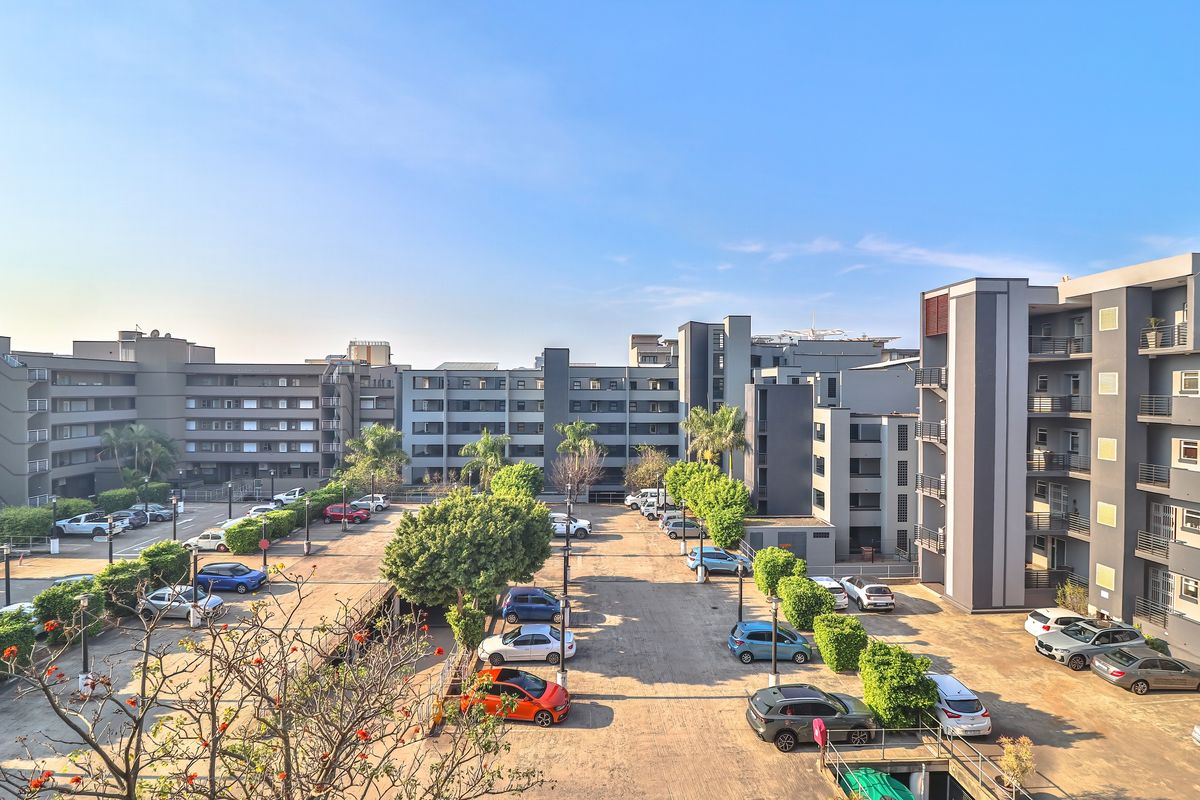 An elevated aerial view of a modern apartment complex featuring paved parking areas and multi-story residential buildings surrounded by landscaped trees.