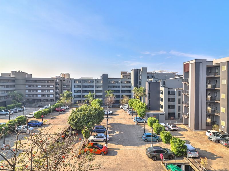 An elevated aerial view of a modern apartment complex featuring paved parking areas and multi-story residential buildings surrounded by landscaped trees.