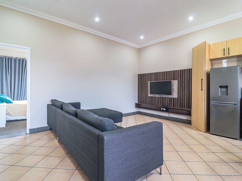 Open-plan living area featuring tiled floors, recessed lighting, and a modern slatted timber feature wall, seamlessly connecting to the kitchen and adjacent bedroom.