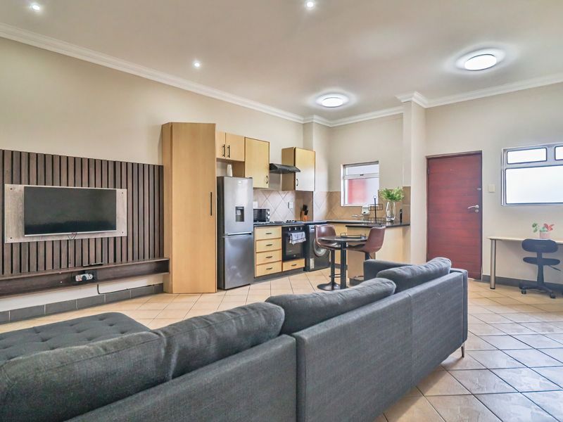 Open-plan living area featuring a modern kitchen with built-in cabinetry, tiled flooring, and a timber slat feature wall with integrated television mount.