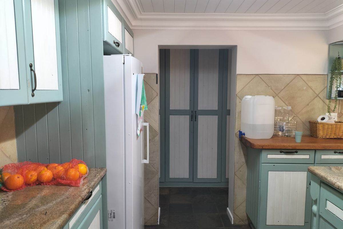 A kitchen featuring painted cabinetry, stone countertops, and a tiled backsplash, leading into a separate storage or utility area with matching doors.