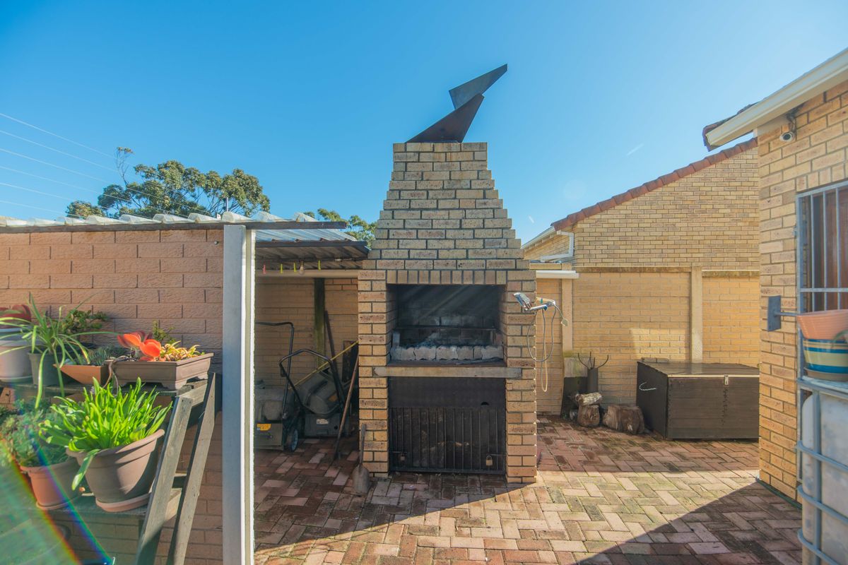 Outdoor paved patio area featuring a built-in brick braai with a metal chimney stack, situated in a private rear courtyard setting.