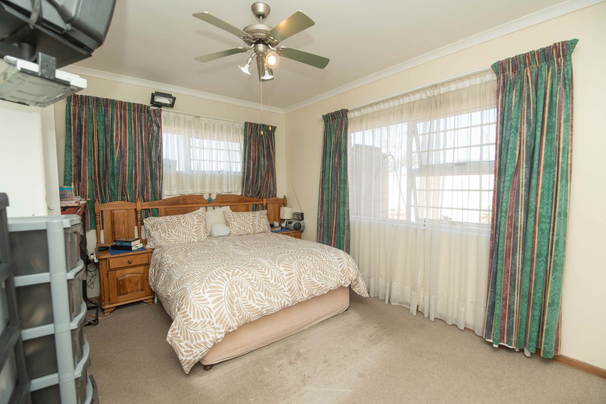 A bedroom featuring a ceiling fan, carpeted flooring, and large windows with security bars, providing natural light and ventilation.