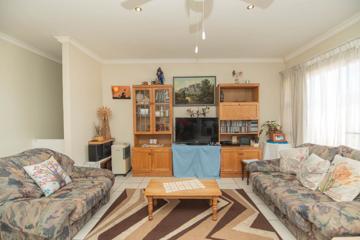 A comfortable living room featuring tiled flooring, crown molding, and a ceiling fan, providing a functional space for relaxation.